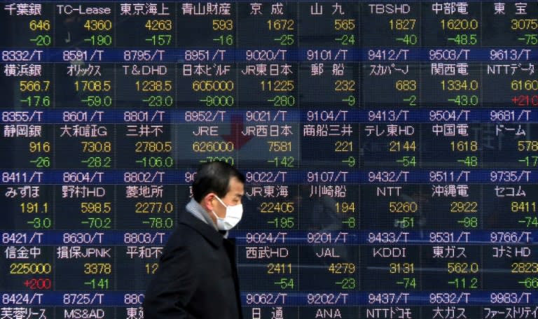 A pedestrian walks past a stock prices board showing numbers of the Tokyo Stock Exchange