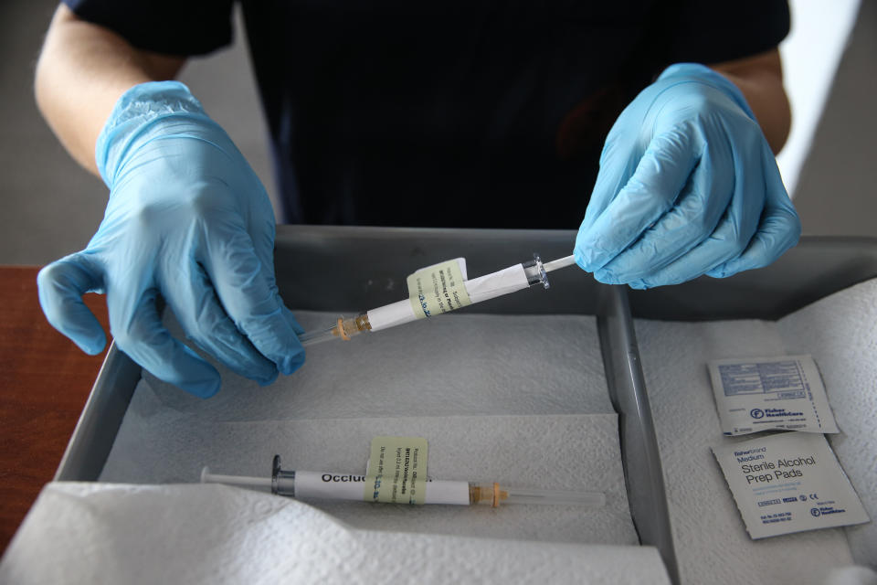 A health care worker wearing blue rubber gloves holds an injection syringe