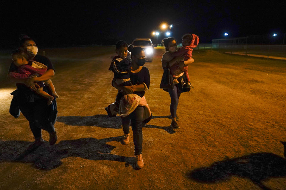 Migrant women carry children in the rain at an intake area after turning themselves in upon crossing the U.S.-Mexico border, late Tuesday, May 11, 2021, in La Joya, Texas. The U.S. government continues to report large numbers of migrants crossing the U.S.-Mexico border with an increase in adult crossers. But families and unaccompanied children are still arriving in dramatic numbers despite the weather changing in the Rio Grande Valley registering hotter days and nights. (AP Photo/Gregory Bull)