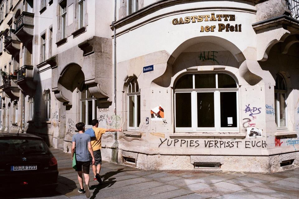 A young man raises his thumb approvingly in the direction of a graffiti reading ‘Yuppies f*** off’ on the wall of a closed restaurant in Dresden (Georg Kussmann/MACK)