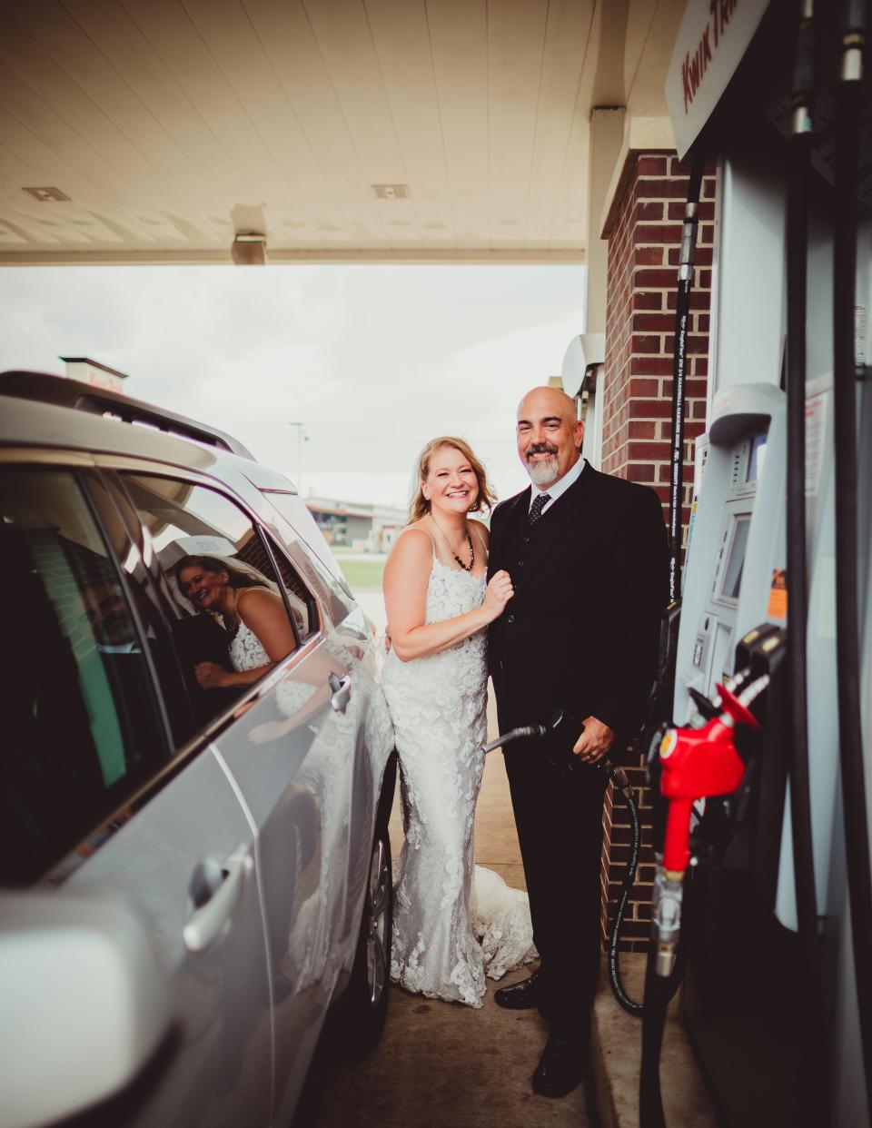 A bride and groom pose at a gas station pump