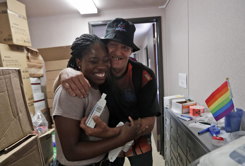 In this Wednesday, July 17, 2019, photo IDEA Exchange social worker Elisha Ekowo, left, is hugged by Michael Ferraro, as he picks up his HIV medication, in Miami. Naida is participating in the University of Miami-sponsored program, which provides HIV-infected homeless people with secure medication lockers or delivers small quantities of medicine to them directly. Naida, who was diagnosed with HIV more than a decade ago, lives underneath a Miami highway overpass and has no safe place to keep her belongings. (AP Photo/Lynne Sladky)