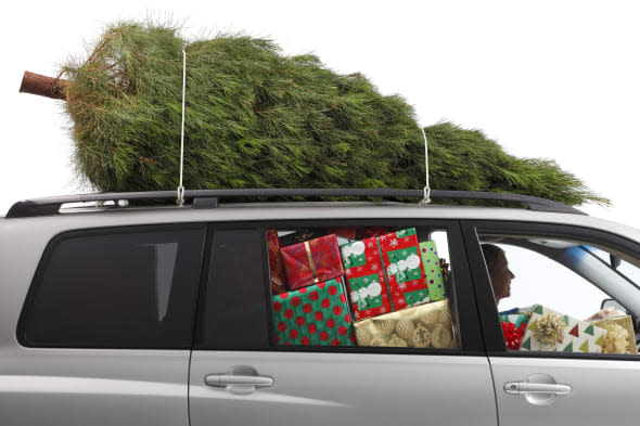 A woman driving a car filled with Christmas presents and a Christmas tree on top..To see more holiday images click on the link b