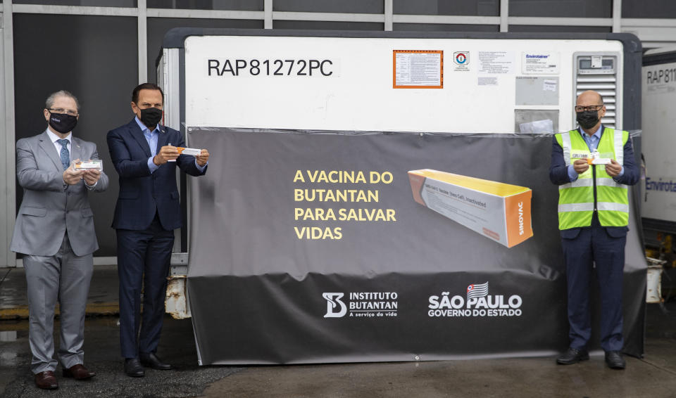 FILE - In this Nov. 19, 2020, file photo, Sao Paulo Governor Joao Doria, second from left, Sao Paulo state Health Secretary Dr. Jean Gorinchteyn, left, and Butantan Institute Director Dimas Covas, right, pose for photos next to a container carrying the experimental COVID-19 vaccine CoronaVac produced by Chinese company Sinovac after it was unloaded from a cargo plane that arrived from China at Guarulhos International Airport in Guarulhos, near Sao Paulo, Brazil. With rich countries snapping up supplies of COVID-19 vaccines, some parts of the world may have to rely on Chinese-developed shots to conquer the outbreak. The question: Will they work? (AP Photo/Andre Penner, File)