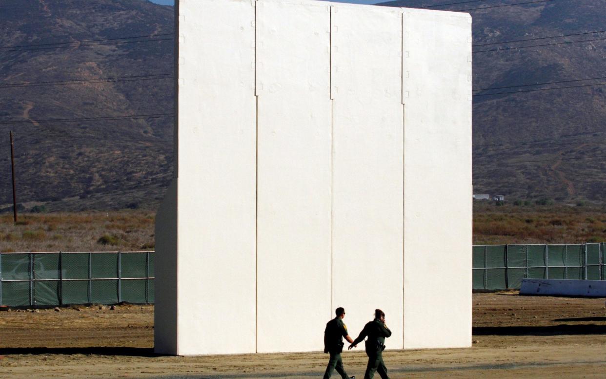 U.S. border patrol officers walk near a prototype for U.S. President Trump's border wall with Mexico, in this picture taken from the Mexican side of the border, in Tijuana - REUTERS