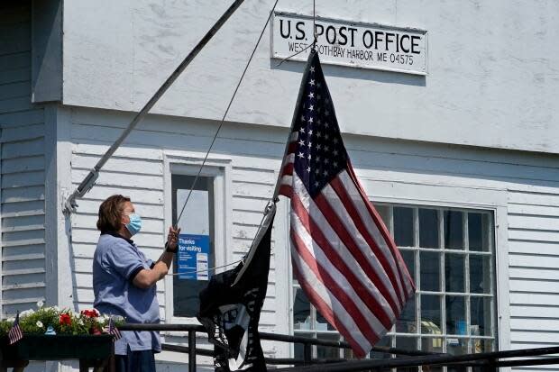 An employee raises the American flag outside a branch of the U.S. Post Office, Wednesday, July 7, 2021, in West Boothbay Harbor, Maine. Many post offices still require the use of face coverings due to COVID-19. (Robert F. Bukaty/The Associated Press - image credit)