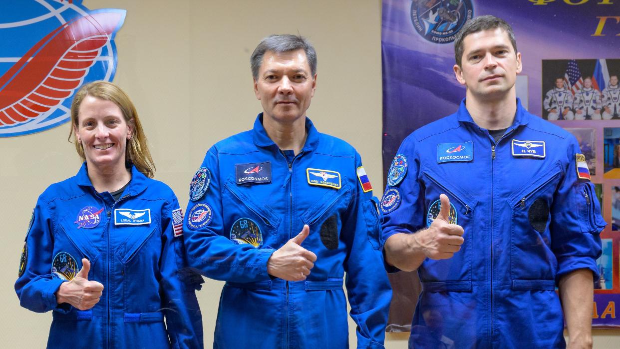  three astronauts - two men and a woman, stand in blue flight suits giving thumbs up 