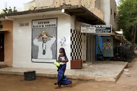 A woman holds her child while walking past the studio of the late, celebrated photographer Malick Sidibe in Bamako, Mali, April 15, 2016. REUTERS/Joe Penney