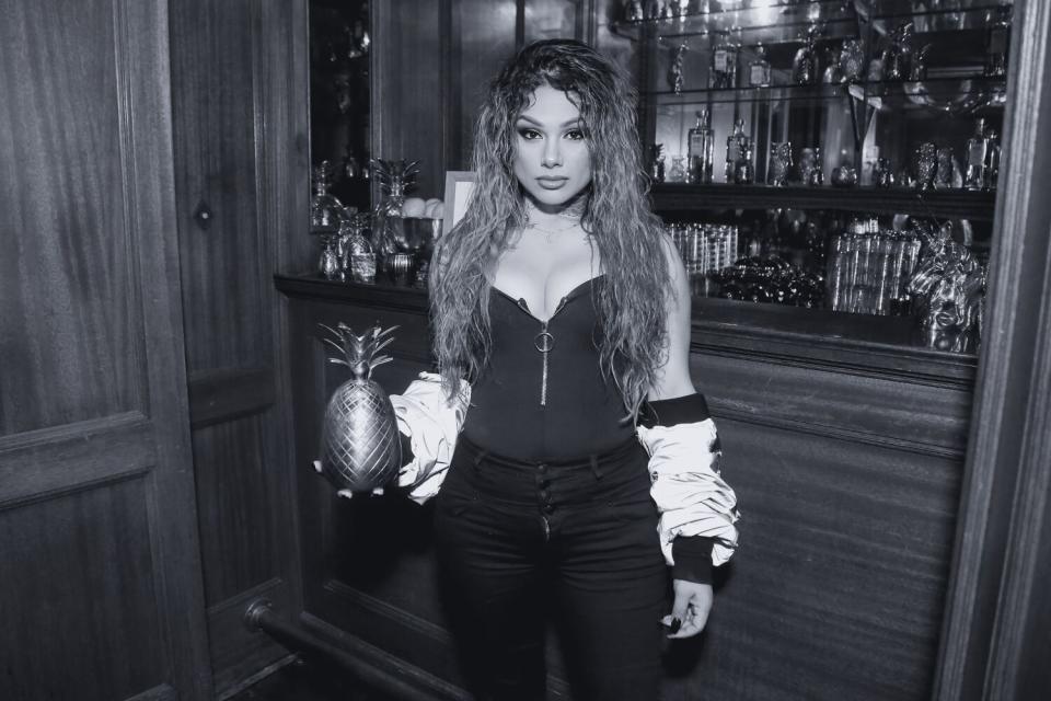 A woman stands with a golden pineapple in front of a bar.