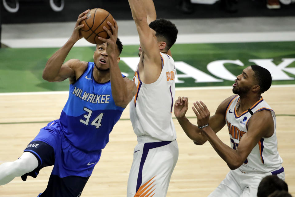 Milwaukee Bucks' Giannis Antetokounmpo, left, drives to the basket against Phoenix Suns' Devin Booker, center, and Mikal Bridges, right, during the first half of an NBA basketball game Monday, April 19, 2021, in Milwaukee. (AP Photo/Aaron Gash)