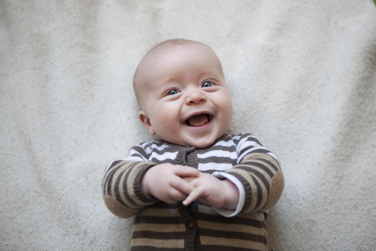 A happy baby smiles and laughs with his mouth open at the camera