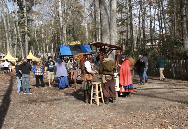 People in medieval costumes at a renaissance fair with tents and attendees in the background