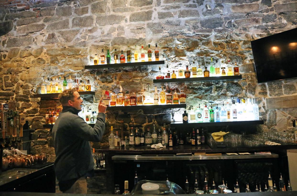 Casey Anderson, owner of the Oar House restaurant in Portsmouth, points out the new bar with a backdrop of a 200-year-old stone wall.