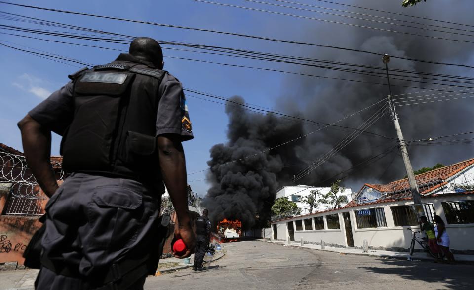 Policemen stand near a burning bus set on fire by residents of the Telerj slum as police attempt to repossess the land in Rio de Janeiro, April 11, 2014. About 5,000 people were evicted by the police after they occupied the site, which belongs to telecoms group Oi, since March 31. REUTERS/Sergio Moraes (BRAZIL - Tags: CIVIL UNREST SOCIETY POVERTY)