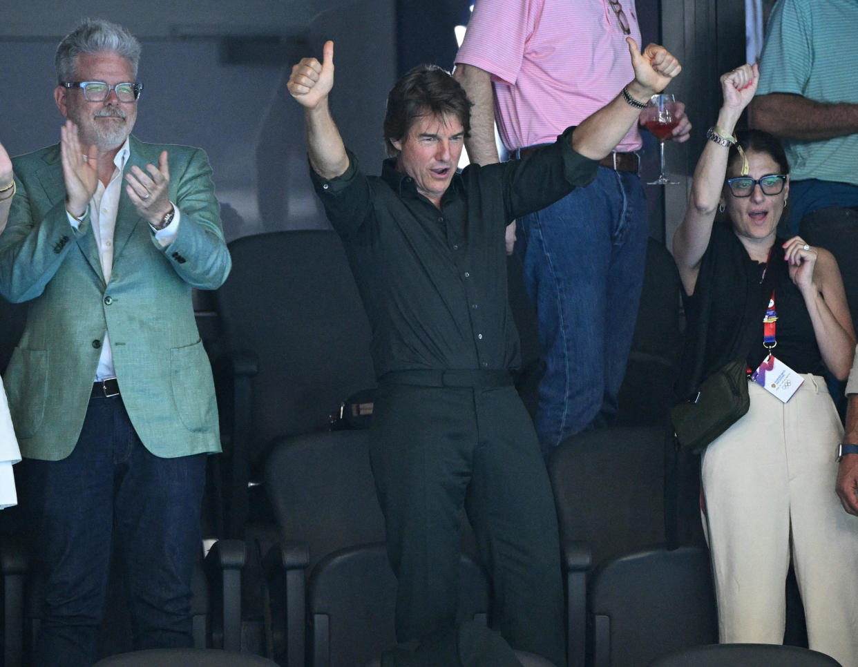 Tom Cruise gives two thumbs-up as he stands in the audience at the Olympics.