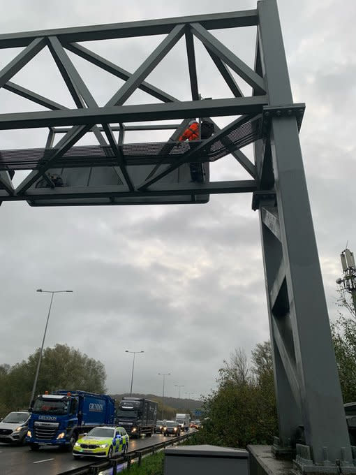 Handout photo taken with permission from the twitter account @SurreyPolice of a Just Stop Oil protester who has climbed a gantry on the M25 between junctions six and seven in Surrey, leading to the closure of the motorway. Surrey Police said the decision was made to close the road 