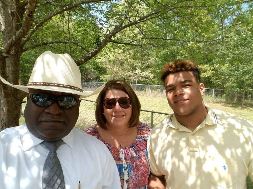 Marc Wilson, right, with his parents, shown outside near a fenced area.