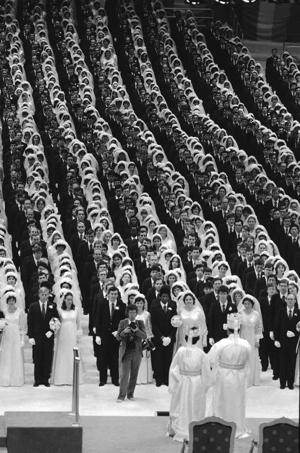 The Rev. Sun Myung Moon and his wife stand before some of the 2,200 couples who were married in New York's Madison Square Garden, July 1, 1982. The bride's dresses were made of identical blue satin and lace while the grooms all wore navy blue suits and red ties. About a third of the couple included men and women of difference races or nationalities, in keeping with the Unification Church's belief that interracial marriages can help end racism.