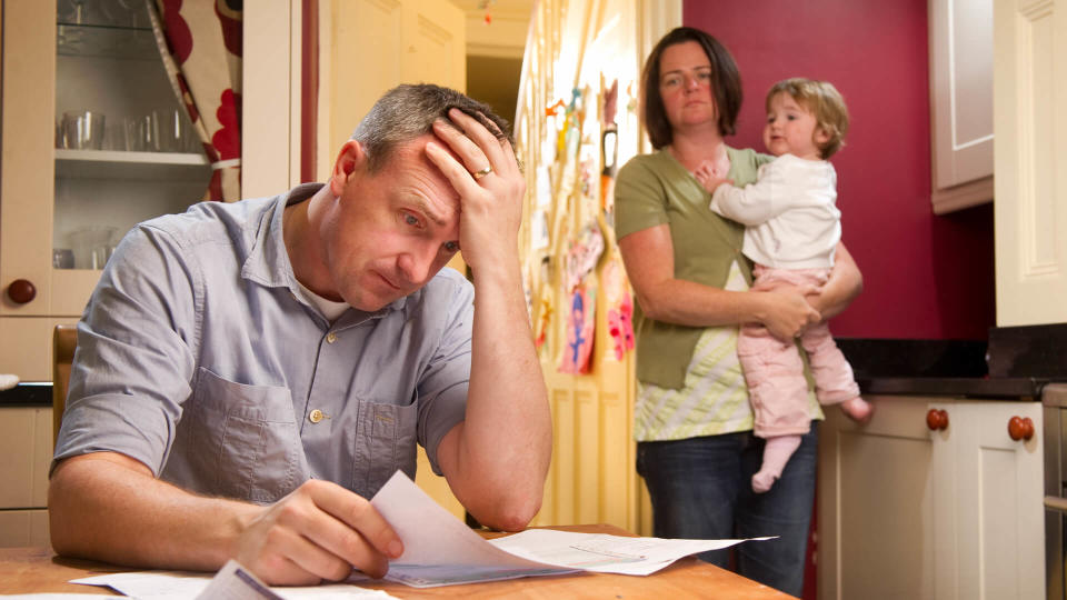 Man stresses over his bill while his wife and child stand in the background.