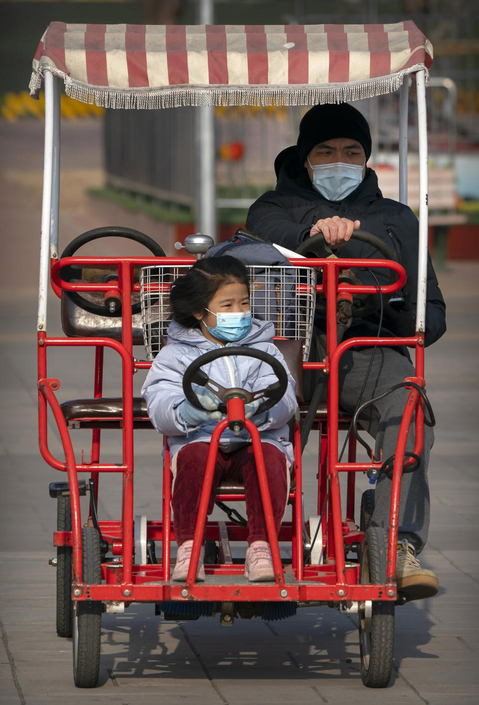 A man and girl wearing face masks to protect against the spread of the coronavirus ride a pedal car at a public park in Beijing, Saturday, Jan. 2, 2021. Wary of another wave of infections, China is urging tens of millions of migrant workers to stay put during next month's Lunar New Year holiday, usually the world's largest annual human migration. (AP Photo/Mark Schiefelbein)