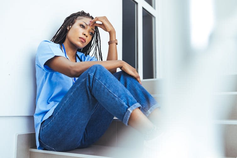 A young female healthcare worker sitting on a staircase, appears despondent.