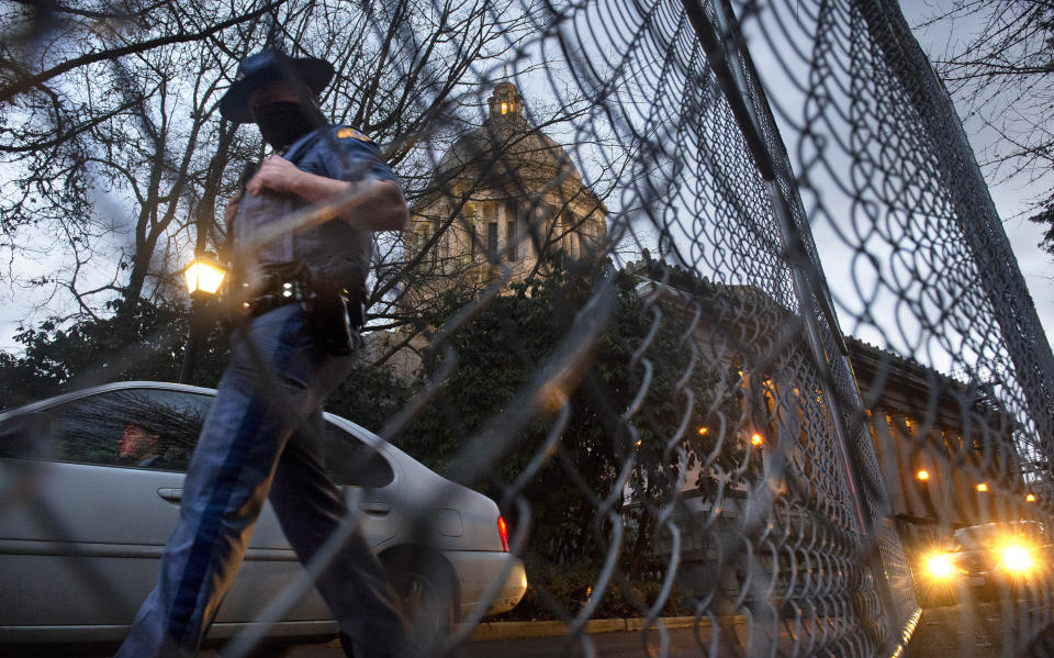 A Washington State Patrol trooper walks past new security fencing installed on Friday, Jan. 8, 2021, around the state Capitol in Olympia, Wash.. in anticipation of the legislative session opening on Monday. (Tony Overman/The Olympian via AP)