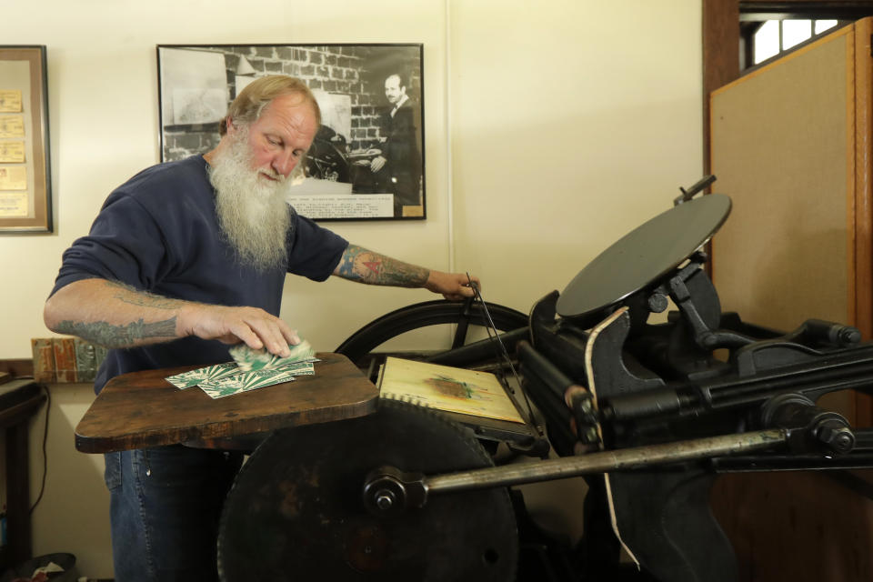 In this May 21, 2020 photo, Loren Ackerman prints wooden money on an 1890s-era press in Tenino, Wash. In an effort to help residents and local merchants alike get through the economic fallout of the coronavirus pandemic, the small town has issued wooden currency for residents to spend at local businesses, decades after it created a similar program during the Great Depression. (AP Photo/Ted S. Warren)