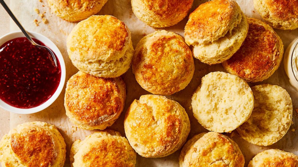 scones on parchment paper with bowls of jam and clotted cream