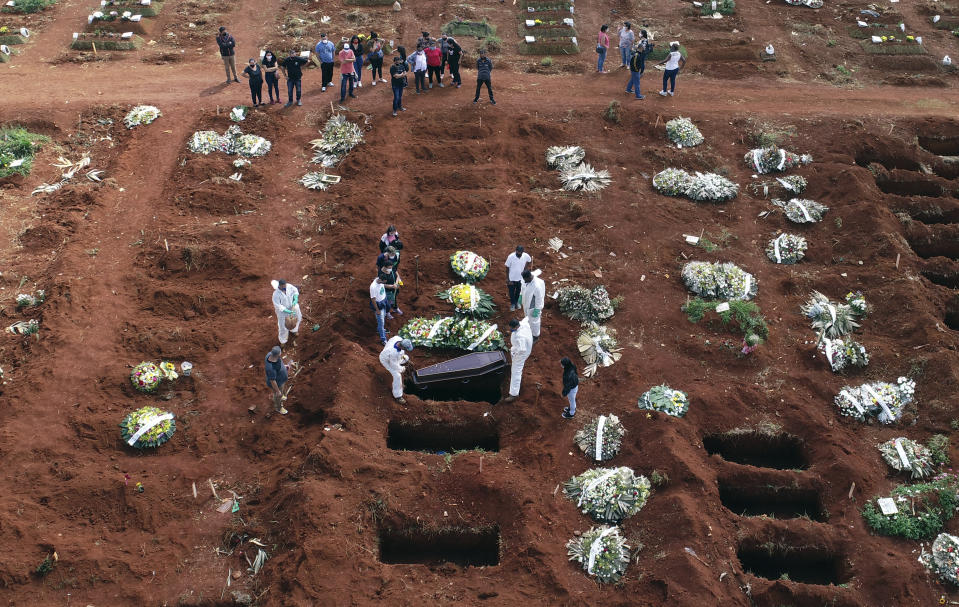 Cemetery workers wearing protective gear lower the coffin of a person who died from complications related to COVID-19 into a gravesite at the Vila Formosa cemetery in Sao Paulo, Brazil, Wednesday, April 7, 2021. The city of Sao Paulo started the daily addition of 600 graves in its municipal cemeteries on Wednesday. (AP Photo/Andre Penner)