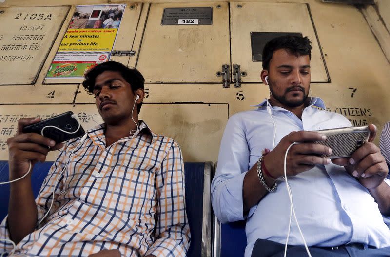 FILE PHOTO: Commuters watch videos on their mobile phones as they travel in a suburban train in Mumbai