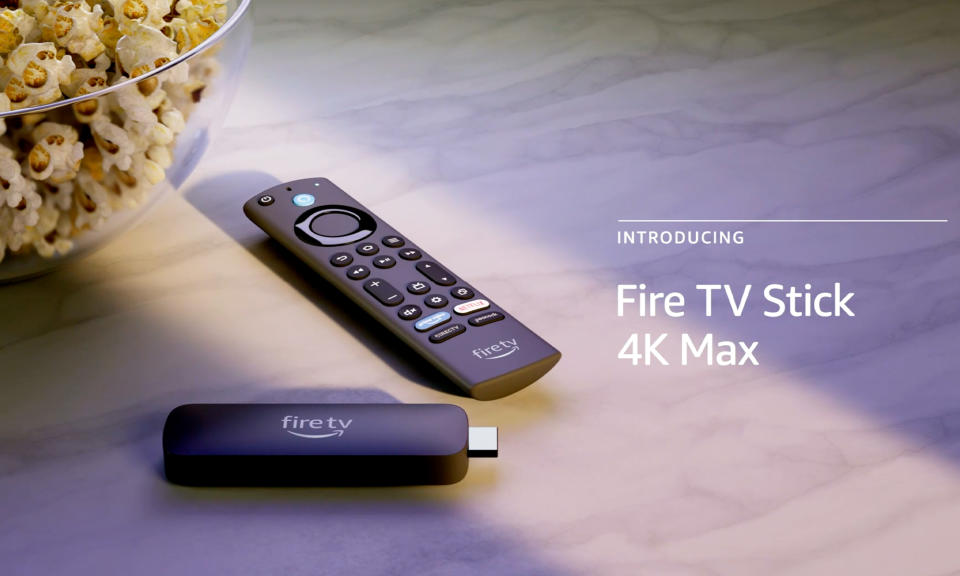 Amazon product photo of the Fire TV Stick 4K Max. The stick-like device sits next to a remote with buttons all over its face. They are on a modern countertop with the edge of a bowl of popcorn visible to the left.