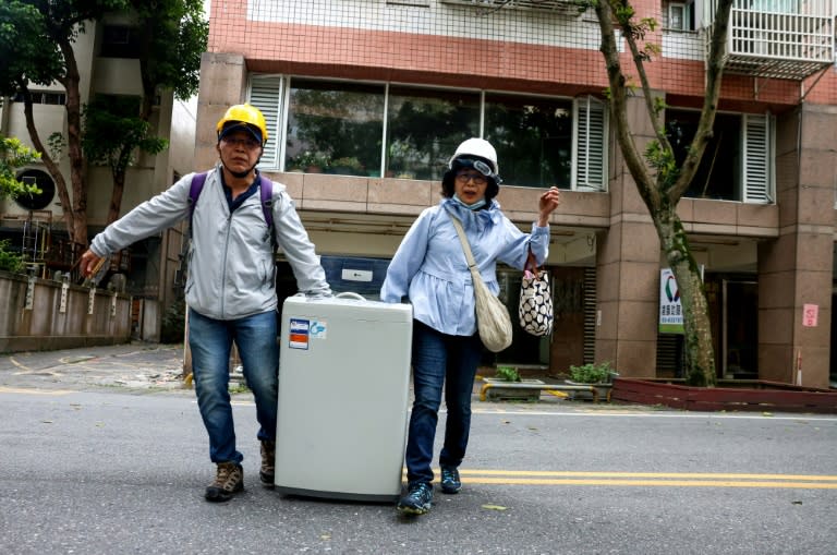 Un couple transportant une machine à laver, extraite d'un bâtiment partiellement endommagé par le séisme du 3 avril 2024 dans la ville de Hualien, à Taïwan (I-Hwa CHENG)