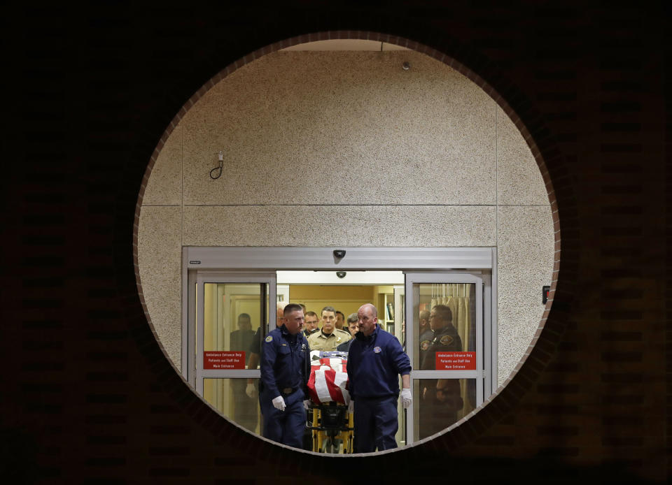 The body of a Kittitas County Sheriff's deputy is draped with a U.S. flag as it is carried out of Kittitas Valley Healthcare Hospital in the early morning hours of Wednesday, March 20, 2019, in Ellensburg, Wash., as seen through a large circular entry window. A sheriff's deputy was killed and a police officer was injured after an exchange of gunfire during an attempted traffic stop. (AP Photo/Ted S. Warren)