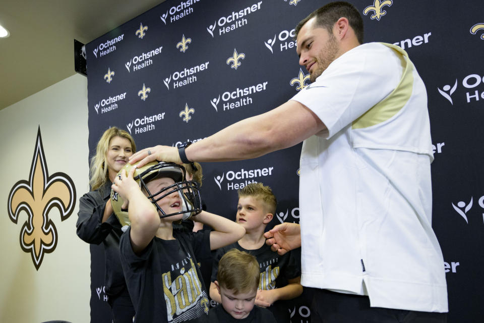 Derek Carr puts a Saints helmet on his son, Dallas Carr, as his wife Heather Carr, left, and other three children look on, as he is introduced as the new quarterback of the New Orleans Saints during an NFL football press conference at the team's training facility in Metairie, La., Saturday, March 11, 2023. (AP Photo/Matthew Hinton)