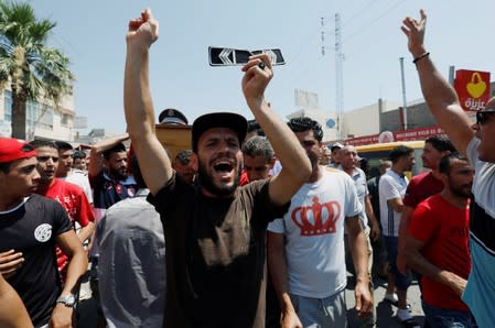 A man holds up a badge as others carry the coffin of a police officer during his funeral in Sidi Hassine