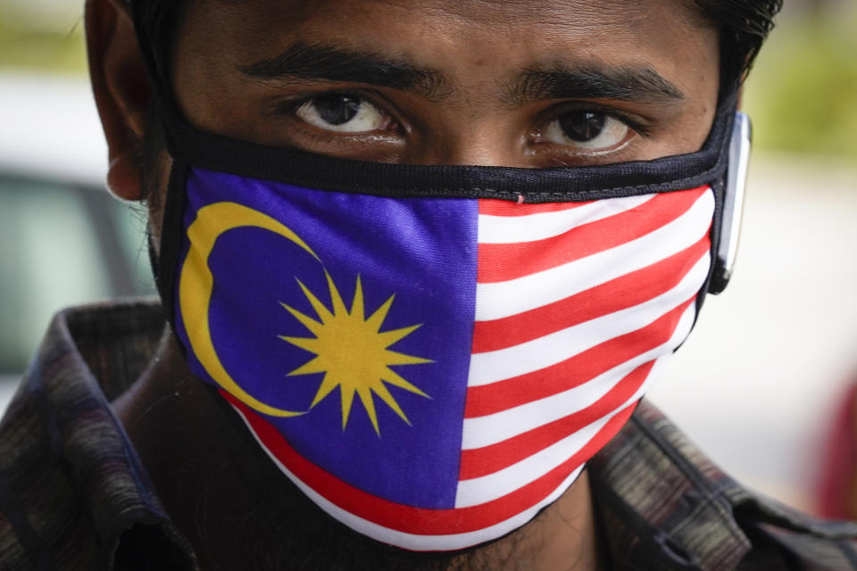 A man wears a mask with Malaysia national flag outside a wet market in downtown Kuala Lumpur, Malaysia, Friday, April 24, 2020. Malaysia, along with neighboring Singapore and Brunei, has banned popular Ramadan bazaars where food, drinks and clothing are sold in congested open-air markets or road-side stalls. The bazaars are a source of key income for many small traders, some who have shifted their businesses online. (AP Photo/Vincent Thian)