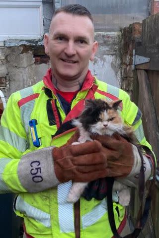 <p>Lancashire Fire and Rescue Service</p> Crew Manager Friar of the Lancashire Fire and Rescue Service holding a grumpy-looking feline he helped rescue