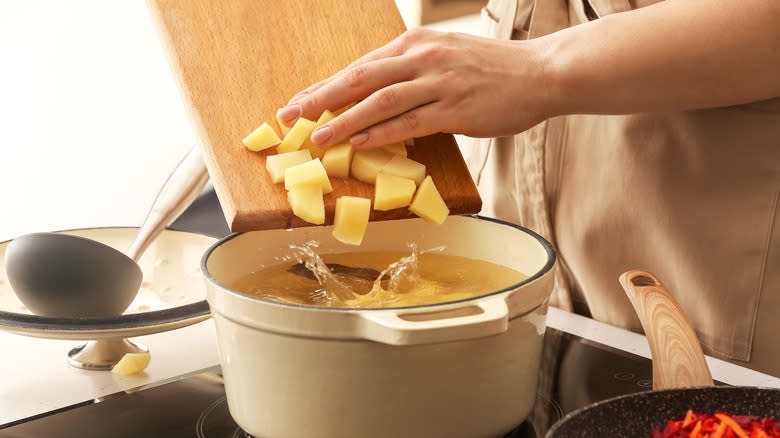 Person pushing chopped potato into pot