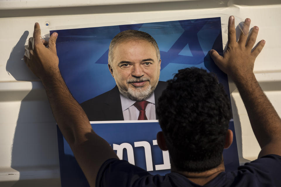 Israeli supporter of the leader of the Yisrael Beiteinu (Israel Our Home) right-wing nationalist party Avigdor Liberman hangs election poster outside the polling station, in the settlement of Nokdim, West Bank, Tuesday, Sept. 17, 2019. (AP Photo/Tsafrir Abayov)