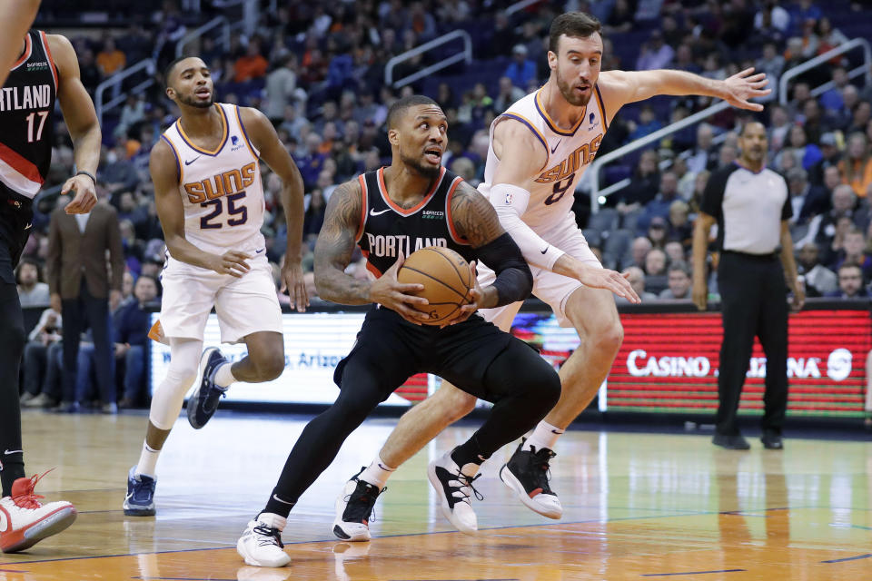 Portland Trail Blazers guard Damian Lillard drives past Phoenix Suns forward Frank Kaminsky (8) and forward Mikal Bridges (25) during the first half of an NBA basketball game, Monday, Dec. 16, 2019, in Phoenix. (AP Photo/Matt York)