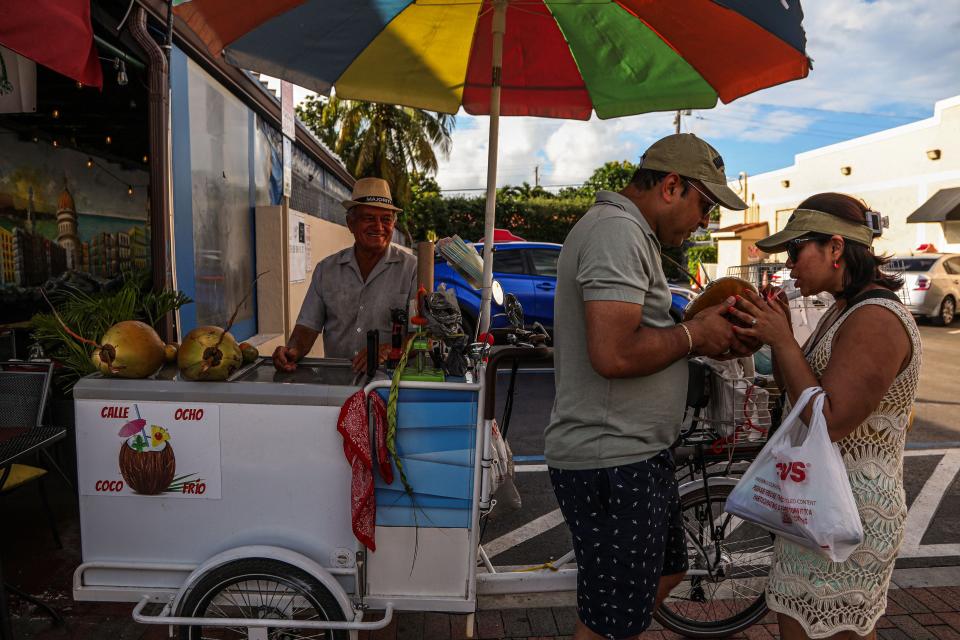 A couple shares their coconut water to cool off from the heat on 8th Street in Little Havana, Miami, Florida during a heat wave on June 26, 2023.