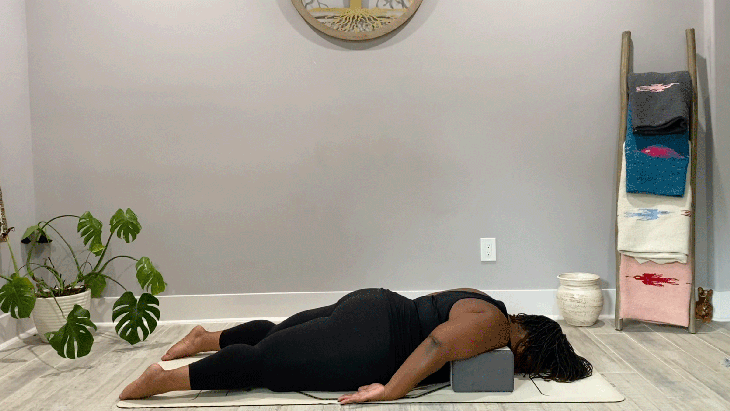 Woman lying on her belly on a yoga mat with blocks beneath her shoulders in supported Locust Pose