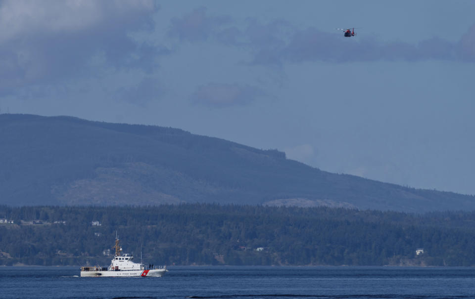A U.S. Coast Guard boat and helicopter search the area Monday, Sept. 5, 2022, near Freeland, Wash., on Whidbey Island north of Seattle where a chartered floatplane crashed the day before. The plane was carrying 10 people and was en route from Friday Harbor, Wash., to Renton, Wash. (AP Photo/Stephen Brashear)