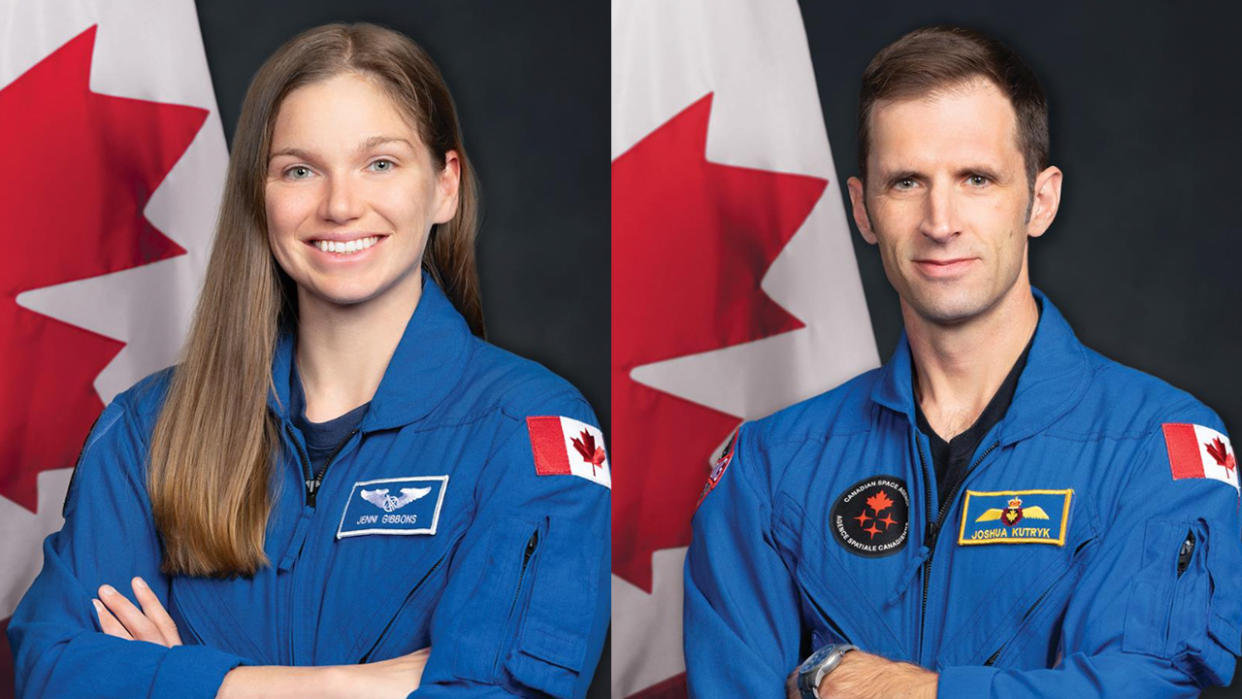  Two astronauts in blue flight suits pose in front of the Canadian flag. 