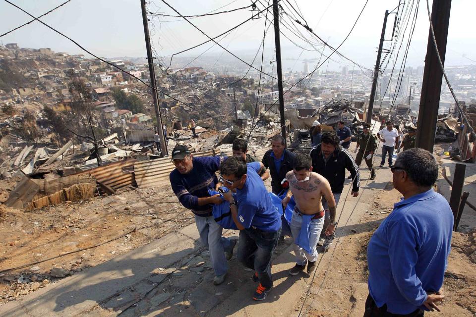 Residents and rescue workers carry a body from the place where a forest fire burned several neighbourhoods in the hills in Valparaiso city