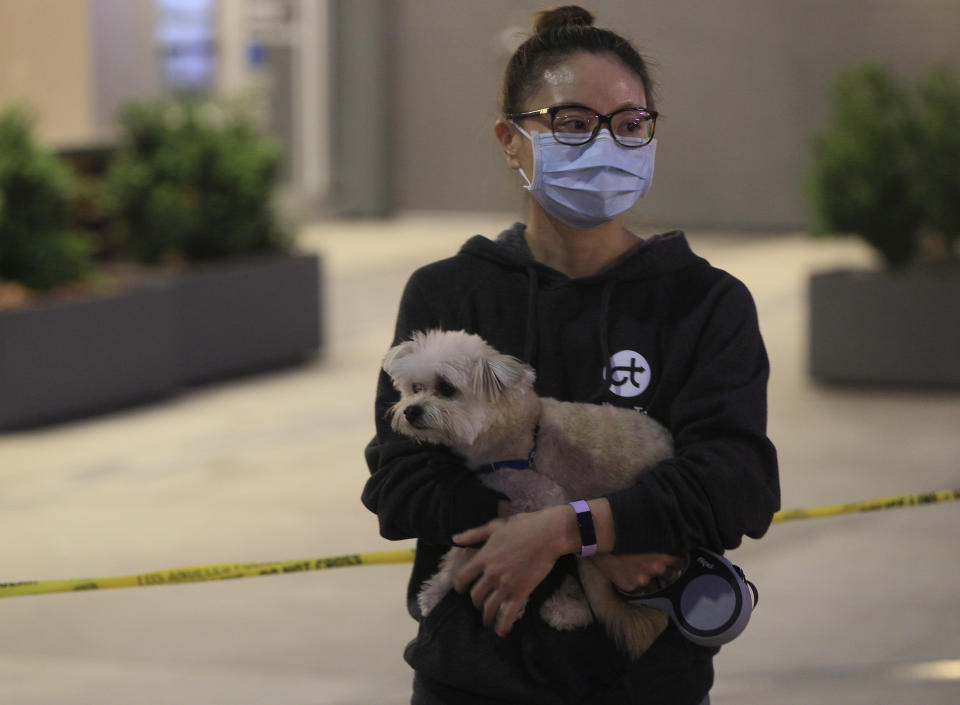 A local resident holds her dog as she watches Los Angeles Fire Department firefighters working the scene of a structure fire that injured multiple firefighters, according to a fire department spokesman, Saturday, May 16, 2020, in Los Angeles. (AP Photo/Damian Dovarganes)