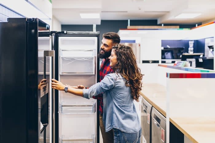 A young couple shopping for a new refrigerator at an appliance store.