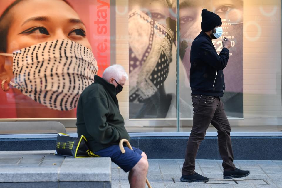 Pedestrian wearing facemasks walk past advertising for facemasks in central Liverpool, north west England on October 14, 2020, as new local lockdown measures come in to force to help stem a second wave of the novel coronavirus COVID-19. - The northwest city of Liverpool -- the only place put into the highest category -- will see a ban on household mixing and pub closures from today for at least four weeks. (Photo by Paul ELLIS / AFP) (Photo by PAUL ELLIS/AFP via Getty Images)