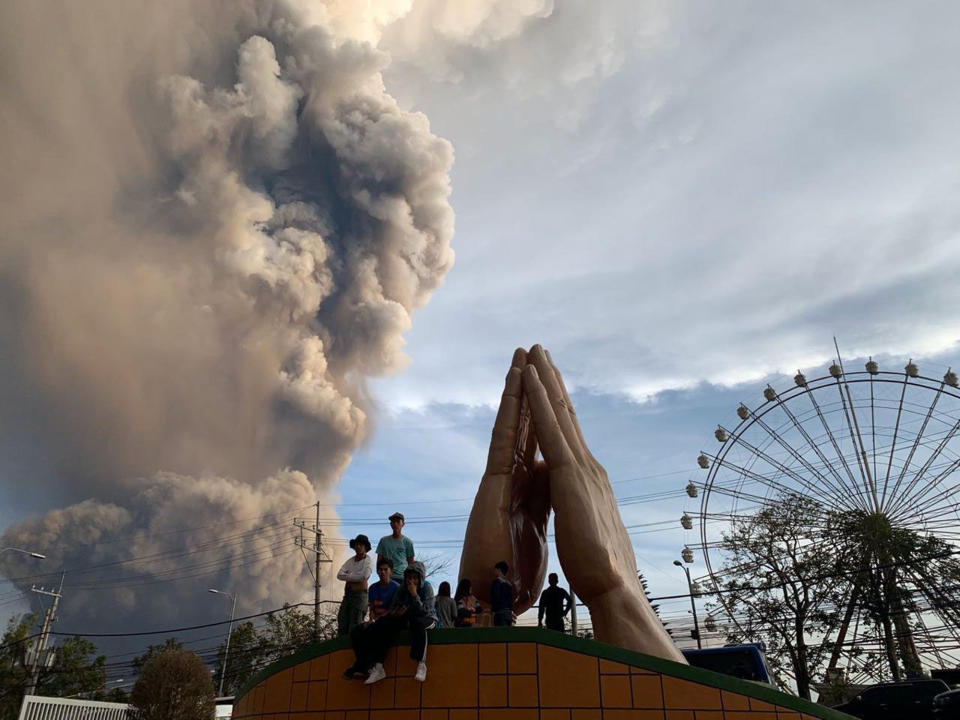 People watch as the Taal volcano spews ash and smoke during an eruption in Tagaytay, Cavite province south of Manila, Philippines on Sunday. Jan. 12, 2020. A tiny volcano near the Philippine capital that draws many tourists for its picturesque setting in a lake belched steam, ash and rocks in a huge plume Sunday, prompting thousands of residents to flee and officials to temporarily suspend flights. (AP Photo/Bullit Marquez)