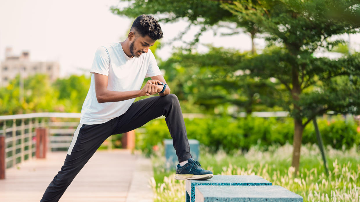  Man stretching and checking GPS watch before run. 